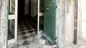 A checkered floor leading to a room with a green door, a metal staircase, and a white wall with a metal pipe. - ANCIENT GENOESE ATTIC (Genova)