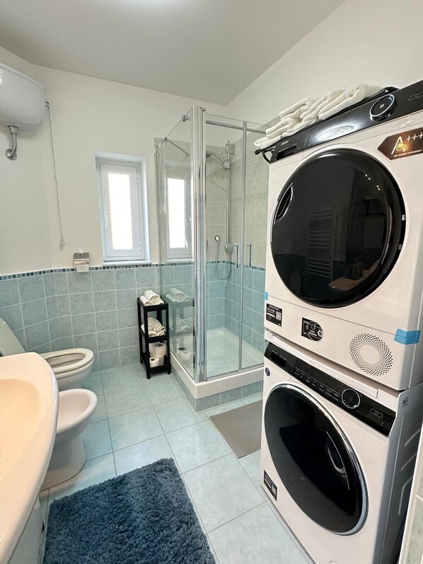 A modern bathroom with a glass-enclosed shower, a built-in washer and dryer, a toilet, and a sink. - ANCIENT GENOESE ATTIC (Genova)