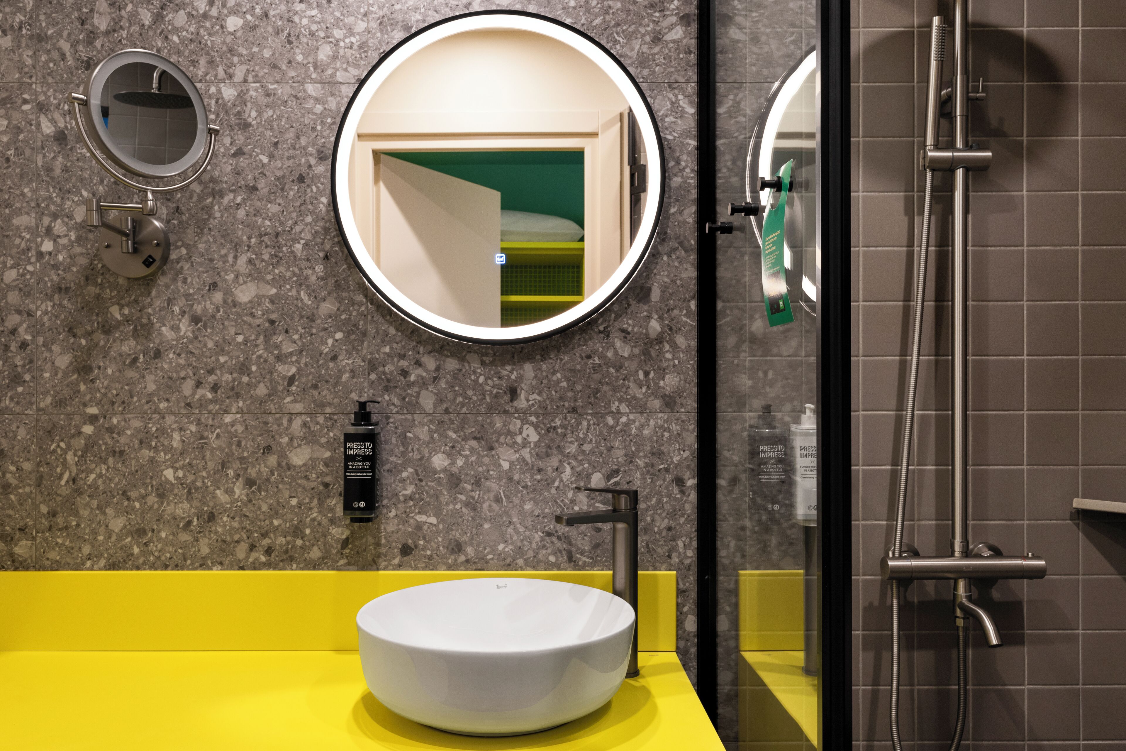 A modern bathroom with a round mirror, a yellow sink, and a shower area.
