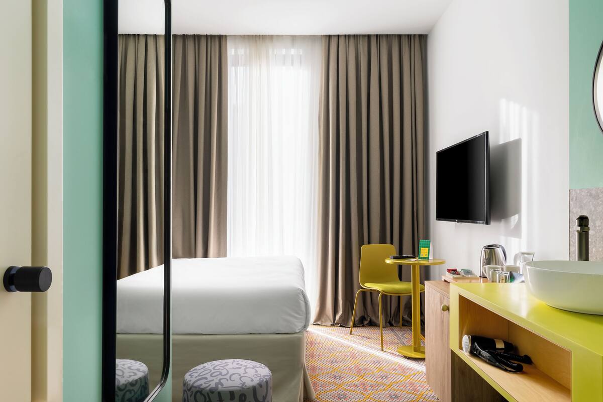 A hotel room with a bed, a TV mounted on the wall, a bathroom with a sink, and a chair.