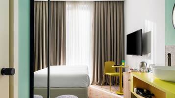 A hotel room with a bed, a TV mounted on the wall, a bathroom with a sink, and a chair.