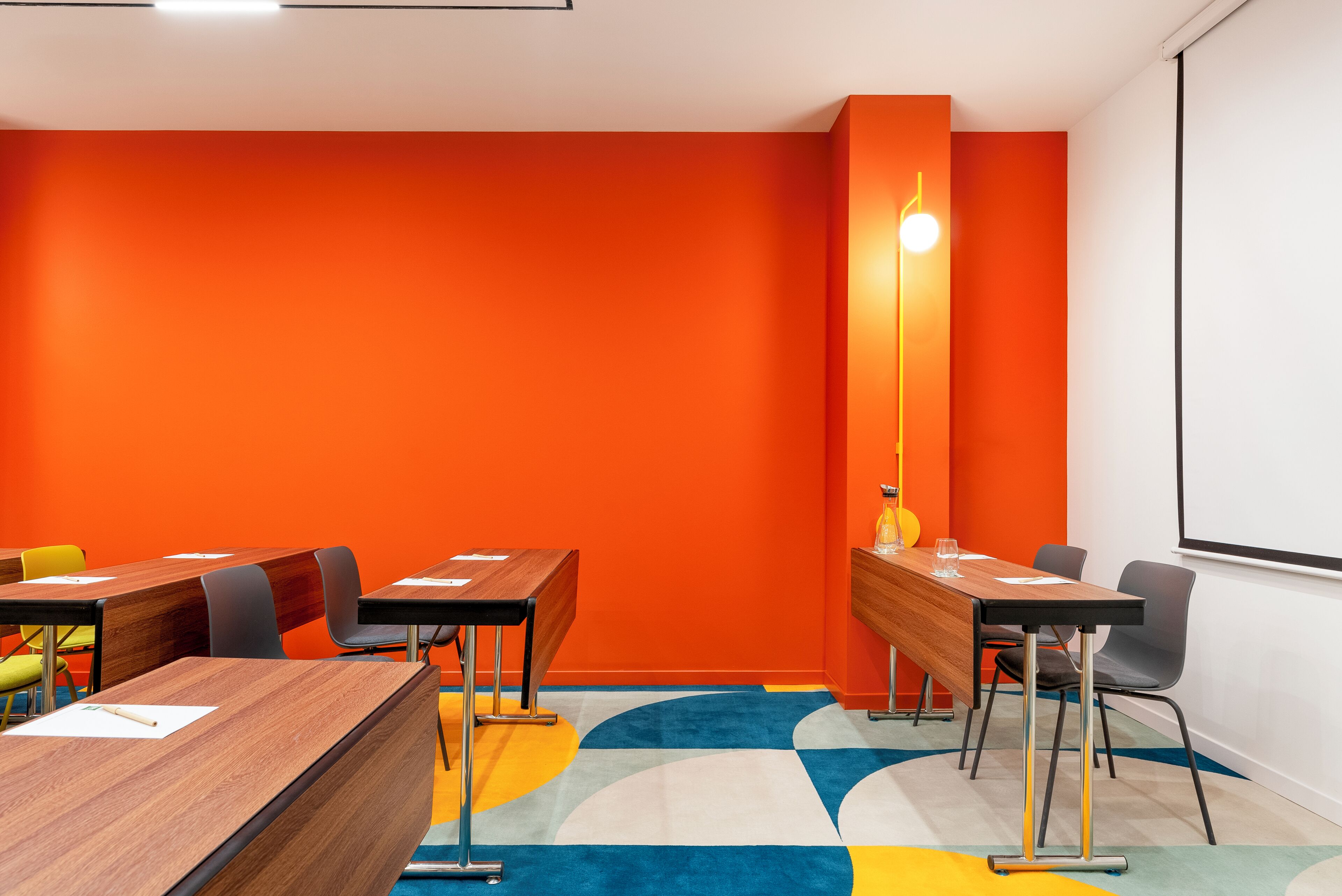 Ein Konferenzraum mit orangefarbenen Wänden, einer großen Stehlampe und einer Projektionsleinwand.