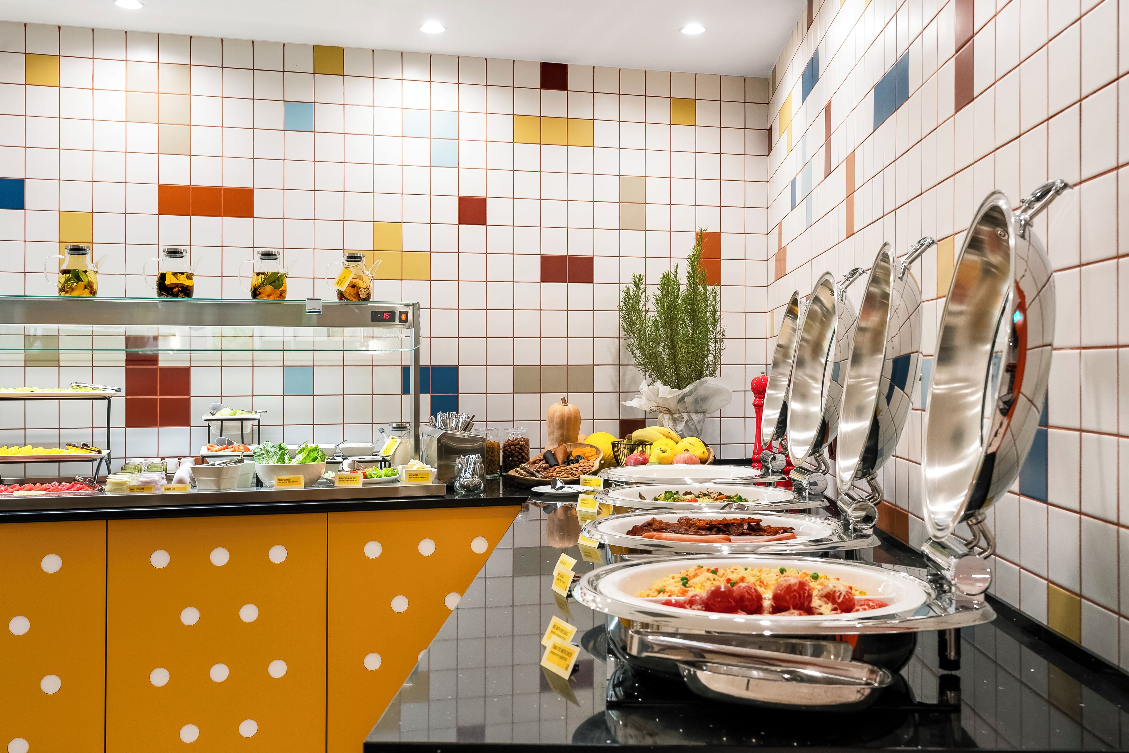 A buffet area with various food stations and a colorful tiled wall.