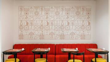 A red sofa with yellow cushions, a wall with a geometric pattern, and tables with black frames and yellow cushions.