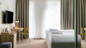 A hotel room with a bed, a desk with a lamp, a chair, a TV, and a window with curtains. - Ibis Styles Old Tbilisi (Tbilisi)