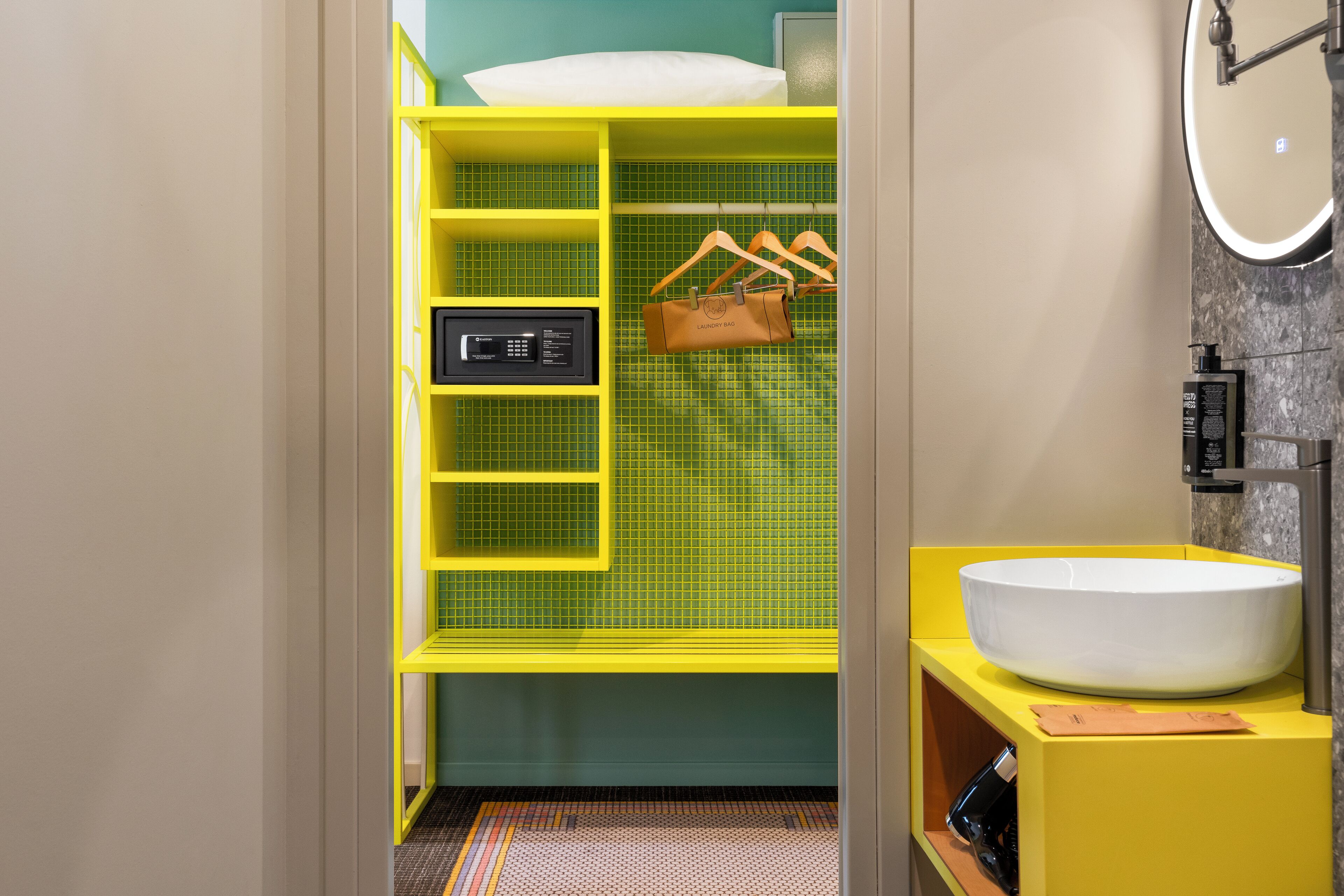 Une salle de bain avec un meuble-lavabo jaune, un lavabo blanc et un mur recouvert de carreaux verts.