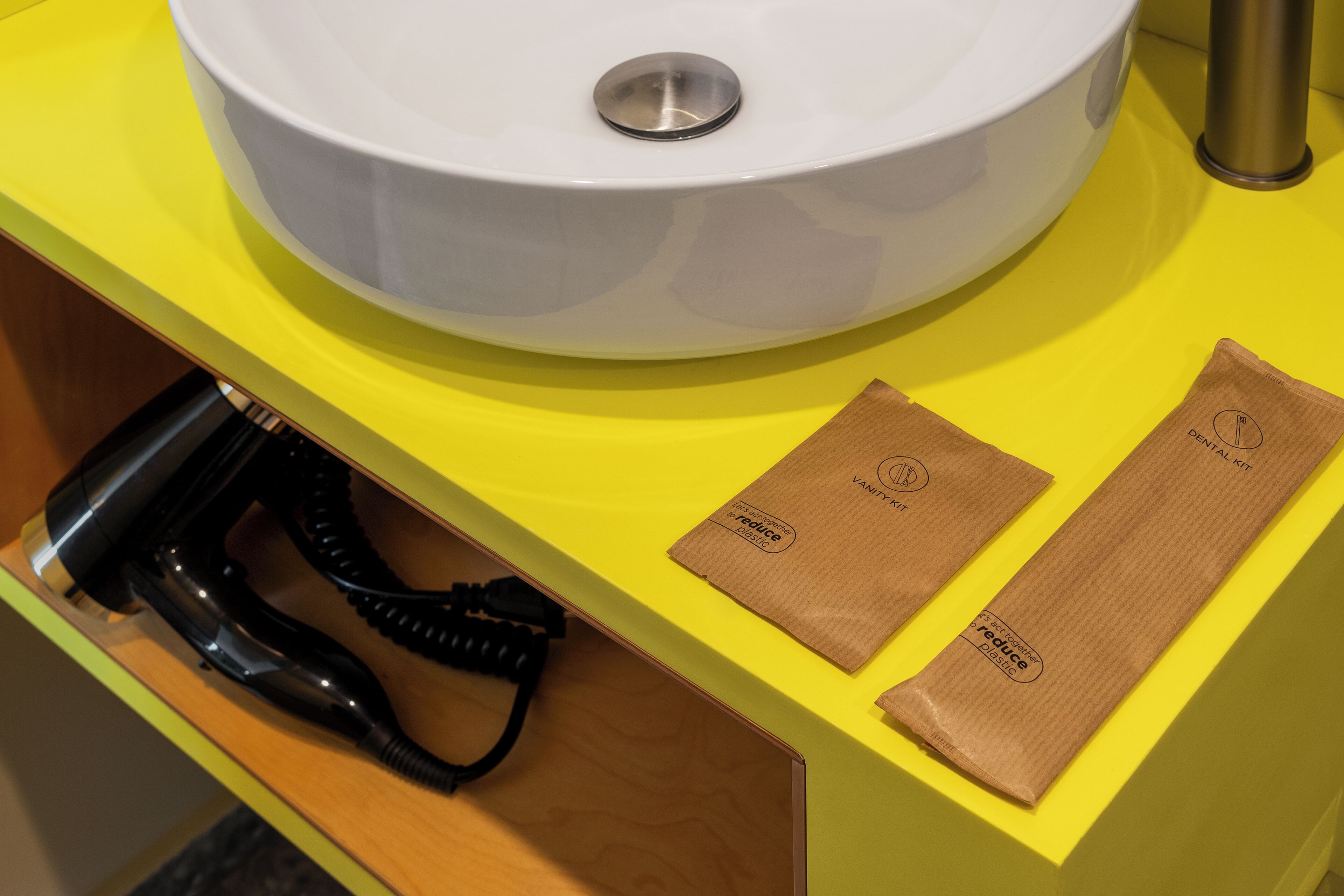 Een badkamer met een witte wastafel, een geel aanrecht en een haardroger in een houten lade.