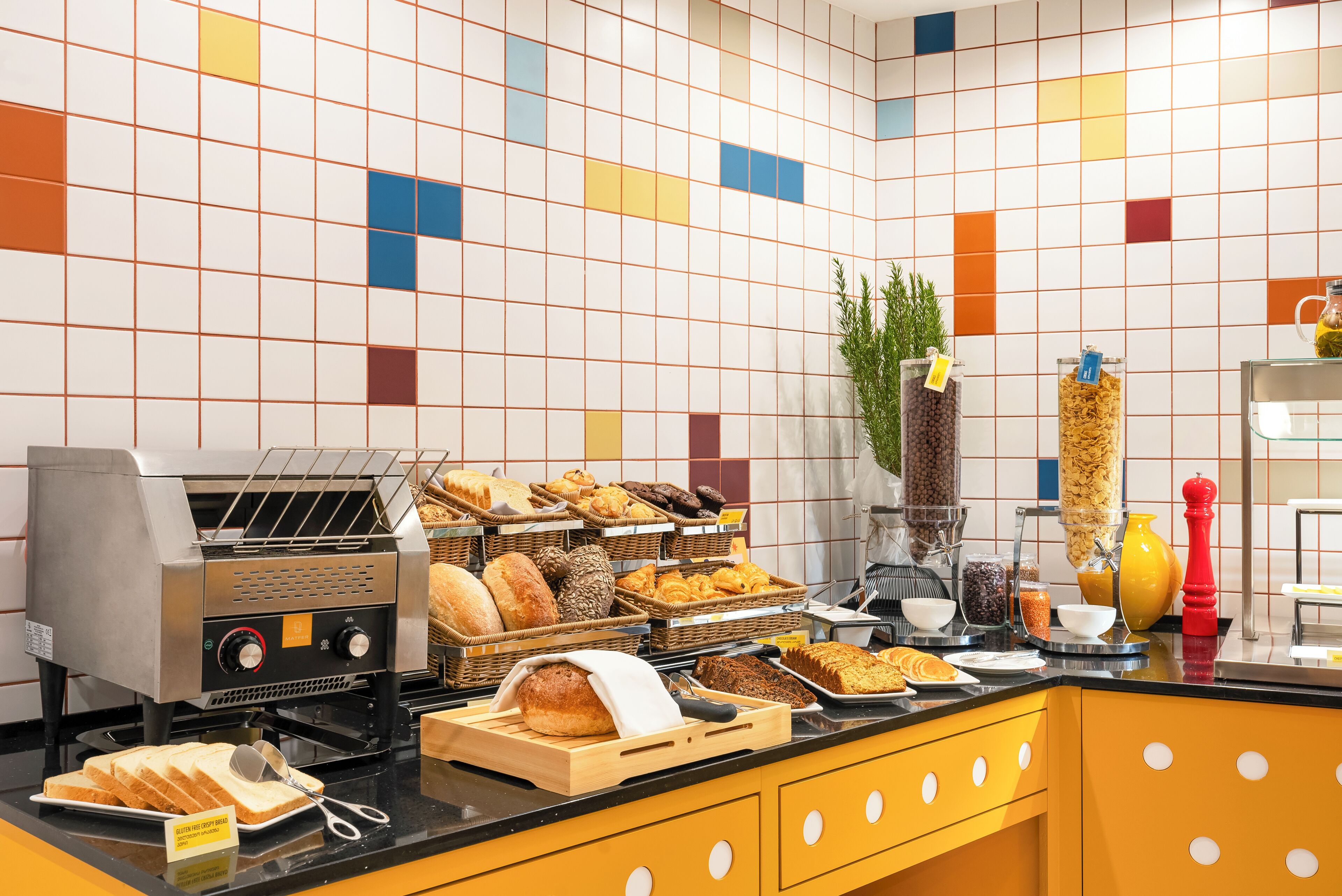 Ein Frühstücksbuffet mit verschiedenen Brotsorten, Gebäck und einer Kaffeemaschine.
