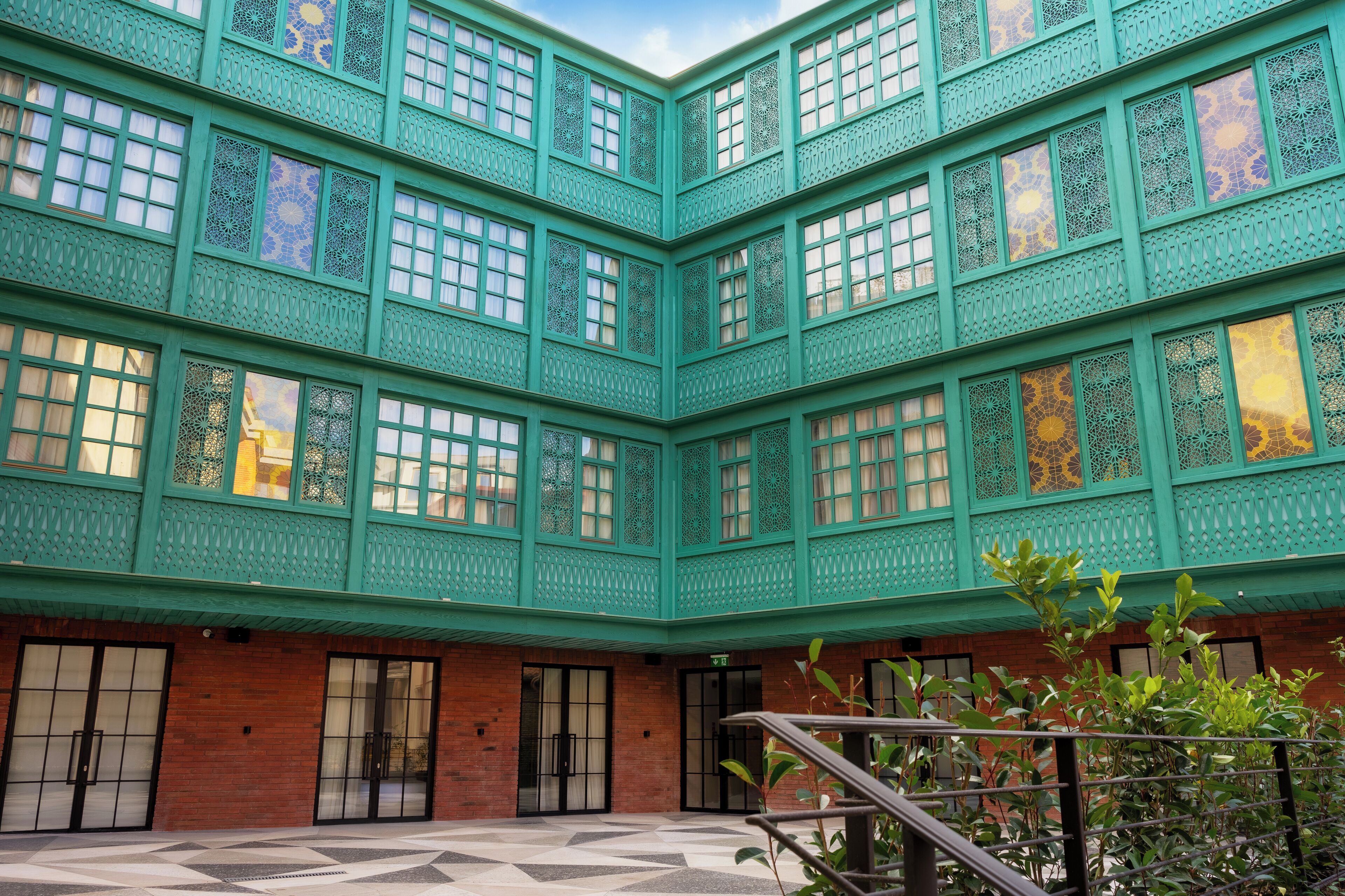 Un immeuble à plusieurs étages, doté d’une façade verdoyante et de fenêtres à motifs.