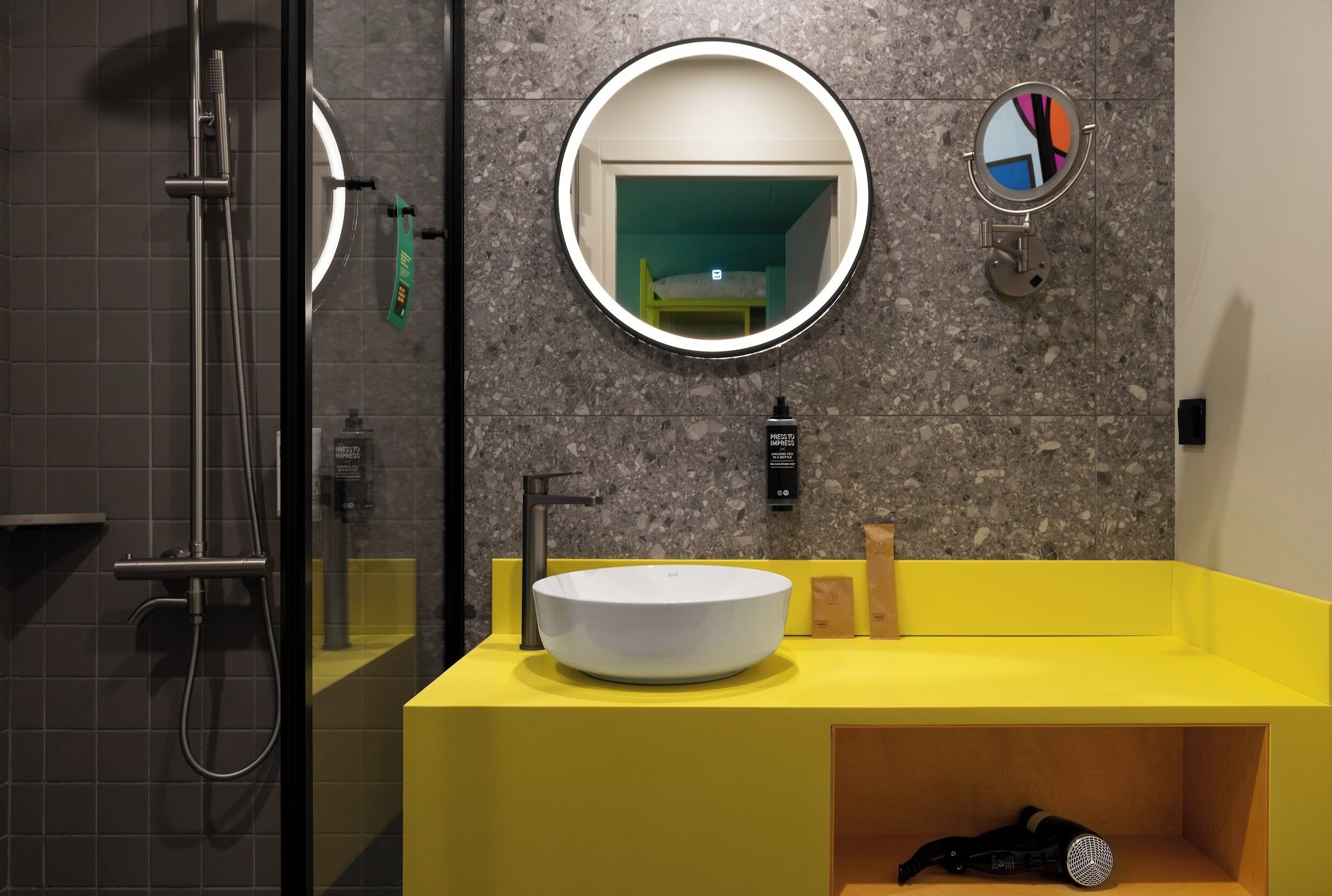 Een moderne badkamer met een ronde spiegel, een geel wastafelmeubel en een douchehoek.