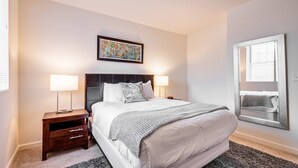 A neatly arranged bedroom with a large bed, two bedside tables with lamps, a framed artwork on the wall, and a large mirror reflecting the room. - Gorgeous Apt with Kitchen (Lexington)