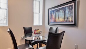 A dining area with a glass table surrounded by four chairs, a bowl of snacks, and a framed painting on the wall. - Gorgeous Apt with Kitchen (Lexington)