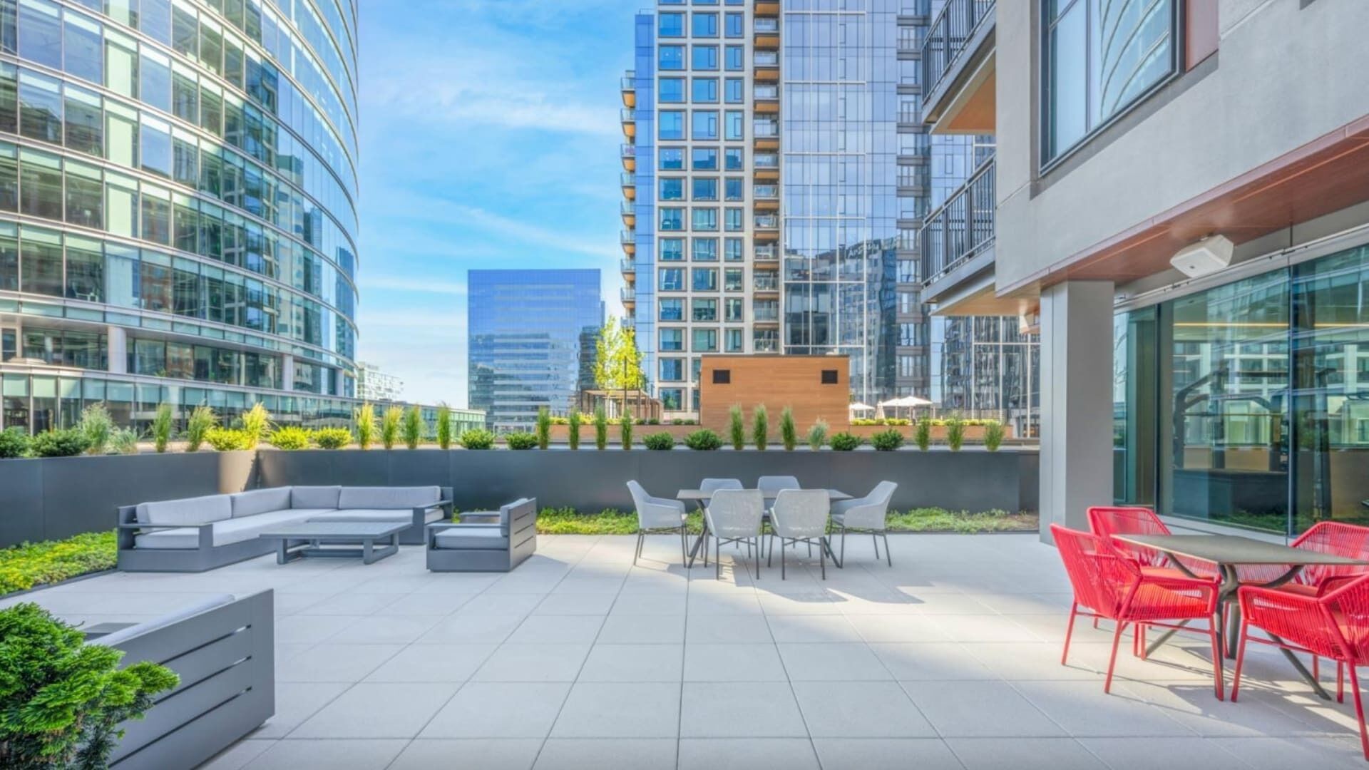 A rooftop patio with modern outdoor furniture, a seating area, and a view of surrounding high-rise buildings.