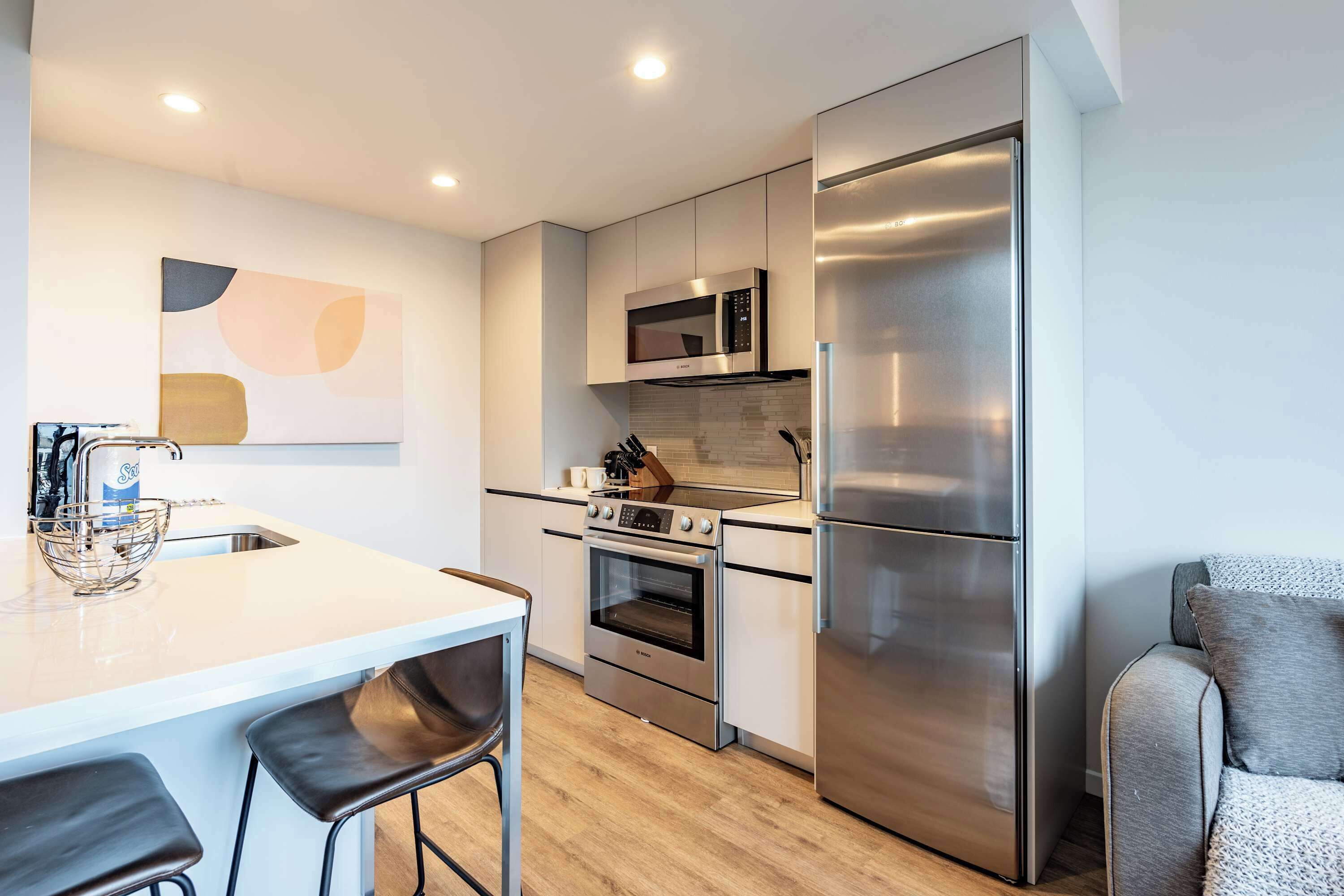 Et moderne køkken med en central ø, rustfrie hvidevarer og et minimalistisk design.