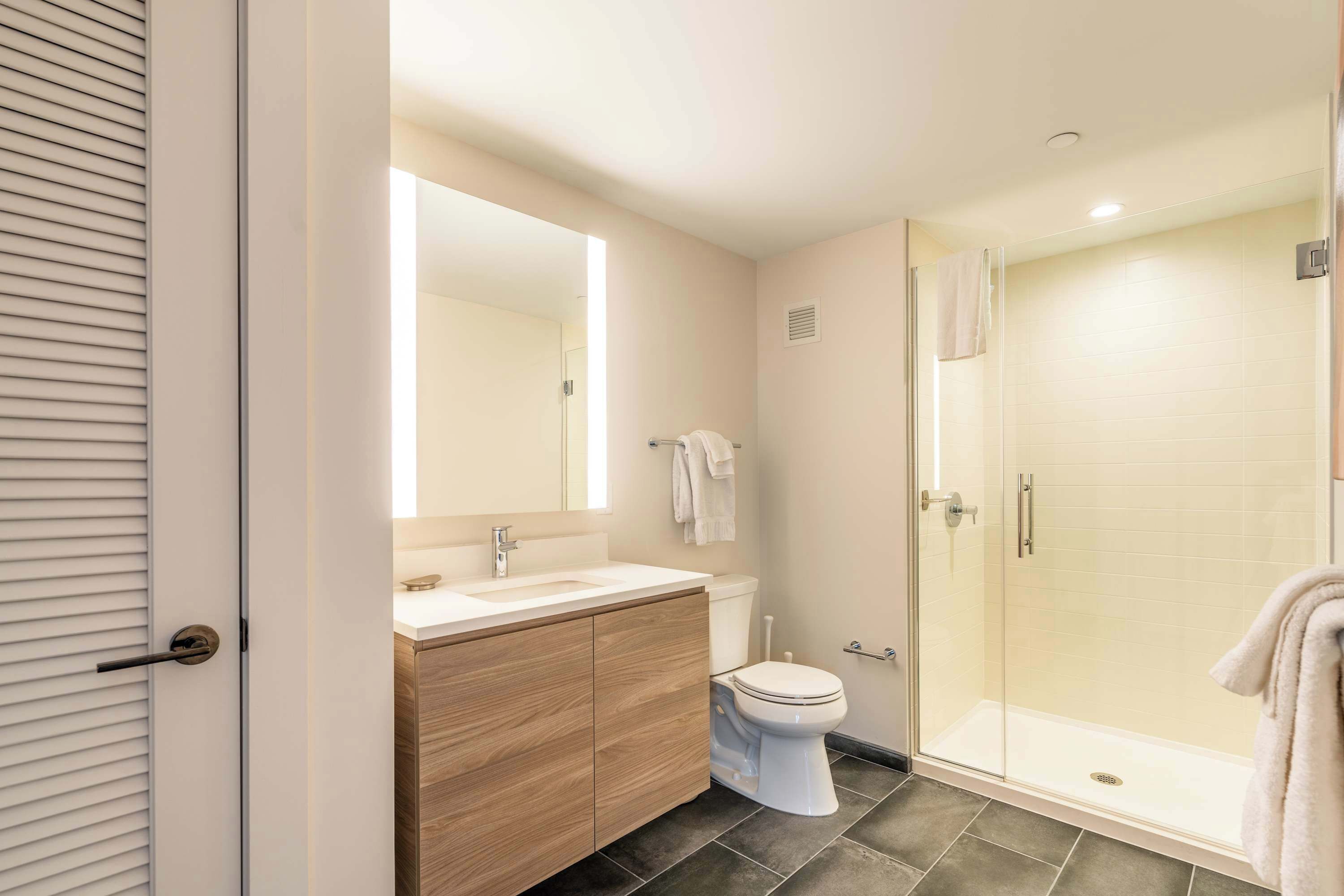 A modern bathroom with a wooden vanity, a toilet, and a glass-enclosed shower.