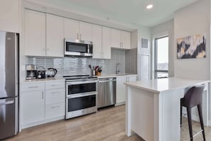 A modern kitchen with white cabinets, stainless steel appliances, and a central island. - Spacious Apt Downtown (Quincy)