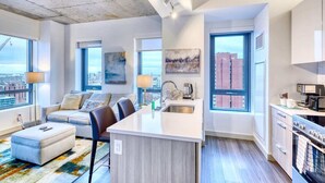 A modern apartment with a living area, kitchen, and large windows offering city views. - Modern Apt In Kendall Square with Gym (Cambridge)