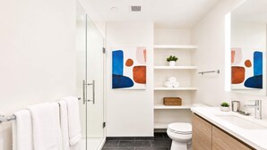 Ein modernes Badezimmer mit Duschabtrennung aus Glas, weißen Fliesen, einer weißen Toilette und einem hölzernen Waschtisch mit Spiegel.