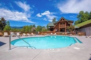 A pool area with lounge chairs and a wooden lodge in the background. - A Cozy Retreat: Unwind, Relax, Repeat (Sevierville)