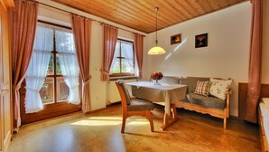 Une pièce chaleureuse avec un plafond en bois, une table à manger sur laquelle se trouve un saladier de fruits, un canapé avec des coussins et une fenêtre avec des rideaux.