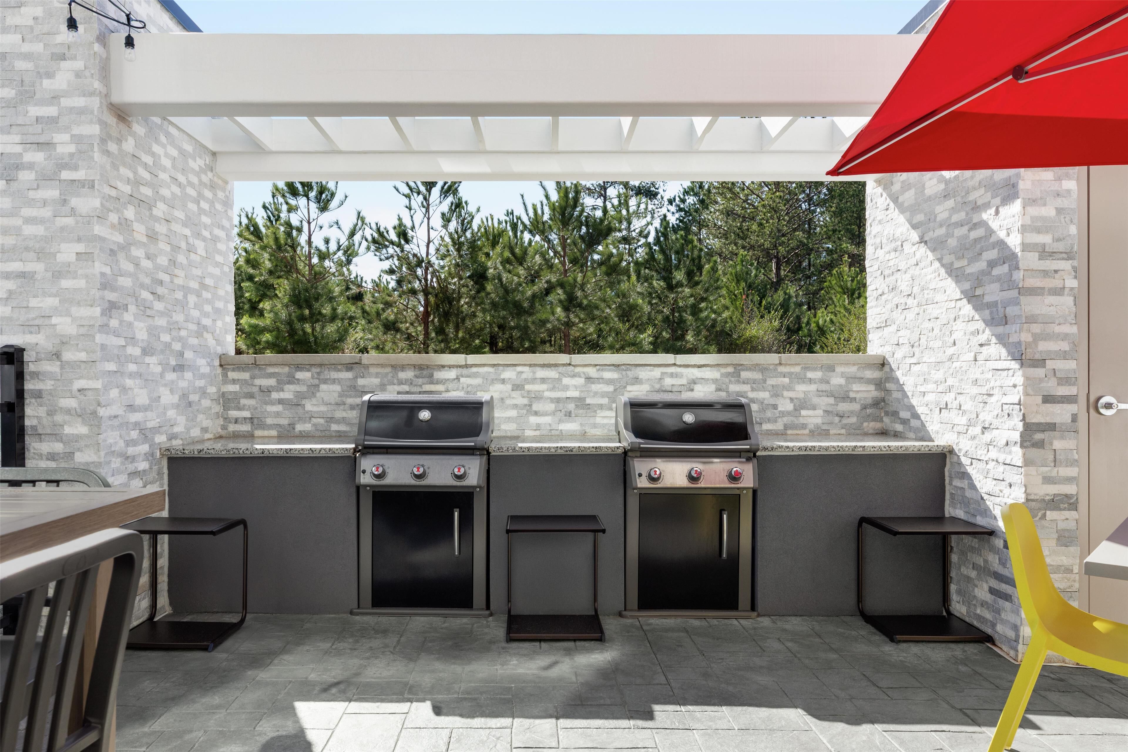 An outdoor kitchen with two gas grills, a wooden table, and a yellow chair.