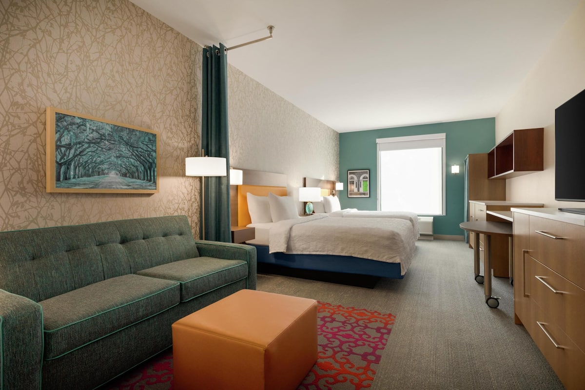 A hotel room with a sofa, a bed, a desk, and a television.
