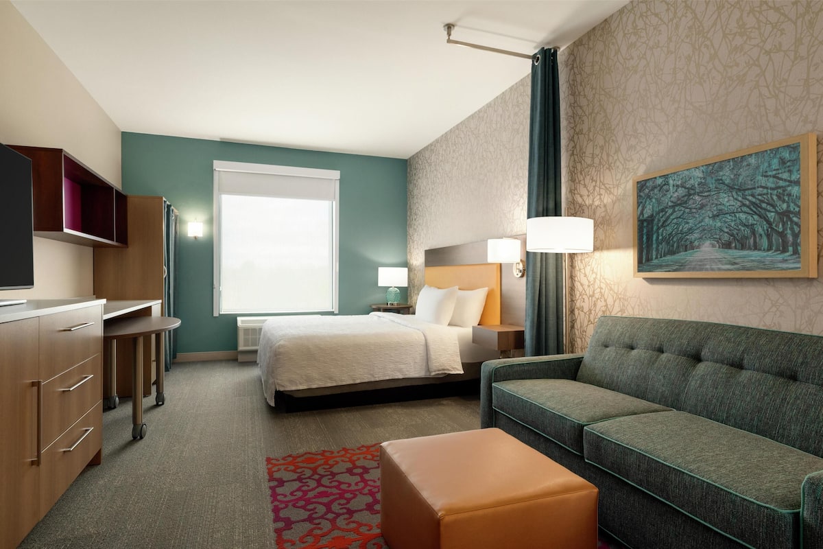 A hotel room with a bed, a sofa, a desk, and a television.