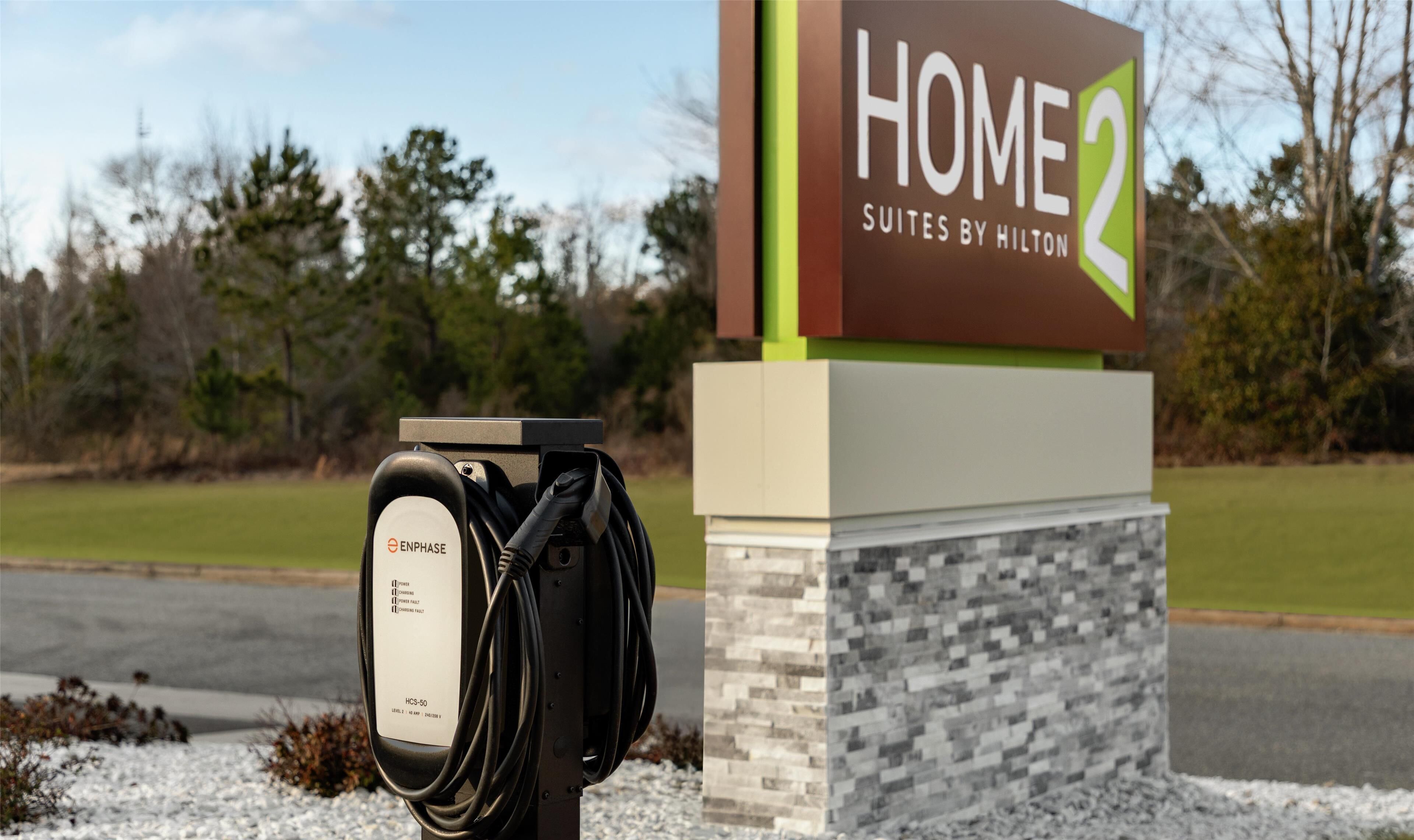 A sign for "HOME 2 Suites by Hilton" with a charging station labeled "ENPHASE" and "HCS-50" in front.
