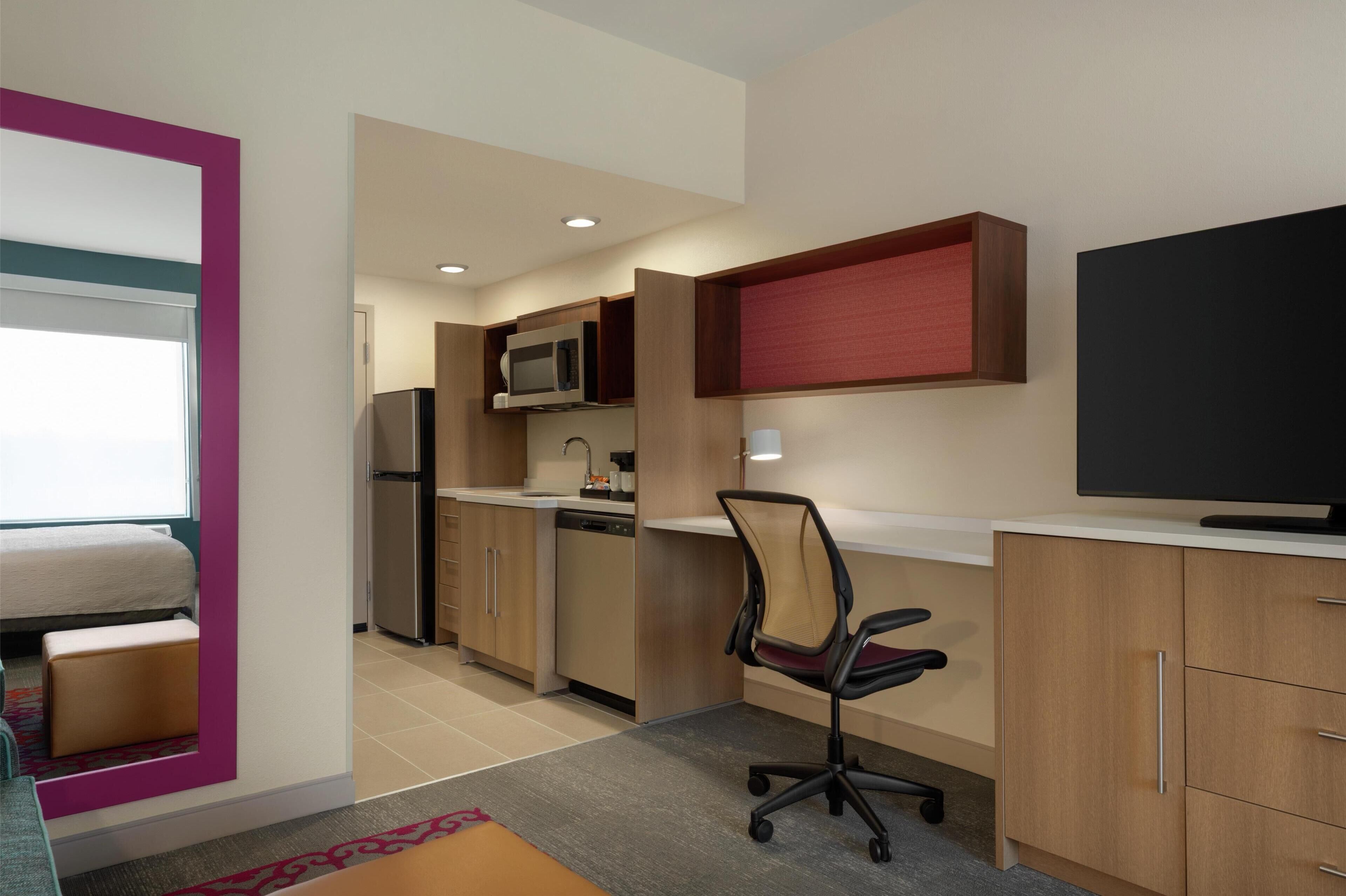 Una habitación de hotel compacta con kitchenette, una cama, un escritorio y televisor.