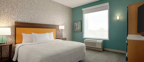 A hotel room with a bed, a nightstand, a lamp, a window with blinds, and a wall-mounted TV.