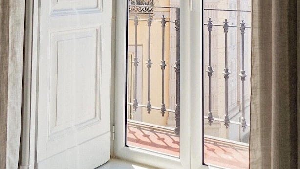 Une pièce dotée d’une grande fenêtre, d’une porte blanche et offrant une vue sur un immeuble avec des balcons.