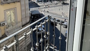 Un balcon orné de balustrades donnant sur une rue animée, avec des bâtiments en arrière-plan.