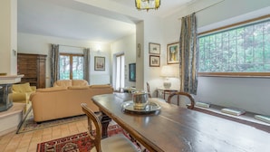 A spacious living room with a wooden dining table, beige sofa, and a fireplace. - Santa Colomba House Nature And Pool (Monteriggioni)