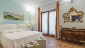A bedroom with a large bed, a dresser, a mirror, and a painting on the wall. - Santa Colomba House Nature And Pool (Monteriggioni)