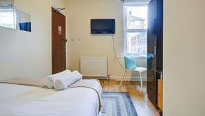 Hotellihuone, jossa on sänky, tuoli, televisio ja ikkuna.