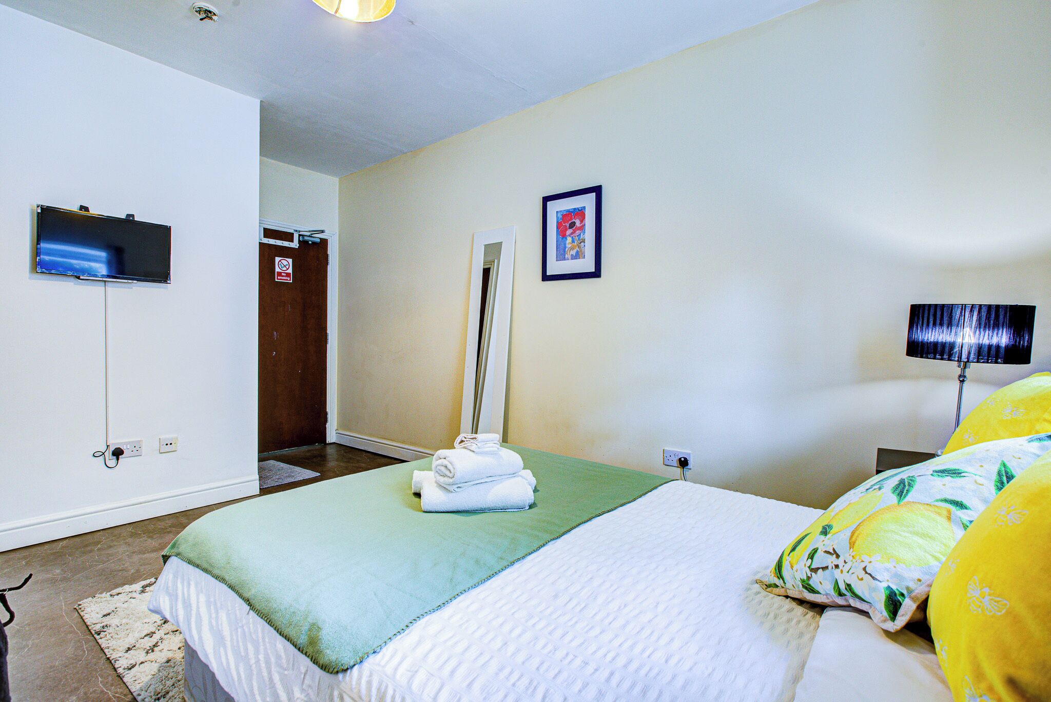 Habitación de hotel con cama, televisor de pantalla plana montado en la pared, puerta con letrero de 'No Pasar' y un cuadro enmarcado en la pared.