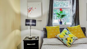 Un dormitorio con una cama, una mesita de noche, una lámpara, una ventana con cortinas y una planta en maceta.