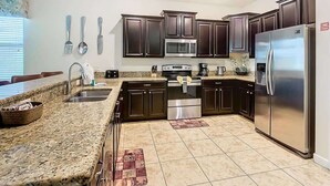 A modern kitchen with dark cabinets, stainless steel appliances, granite countertops, and a central island with a sink. - Palm Paradise Haven (Four Corners)