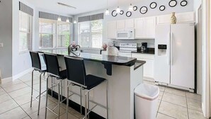 Une cuisine moderne avec des meubles blancs, un îlot central doté de tabourets de bar et un réfrigérateur blanc.