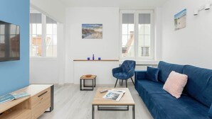 Ein modernes Wohnzimmer mit einem blauen Sofa, einem Holztisch, einem blauen Sessel und einem Fernseher an der linken Wand.