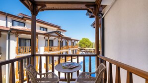 A balcony with wicker chairs and a small table, overlooking a pool and adjacent buildings. - MARVELOUS SARIGERME (Sarigerme)