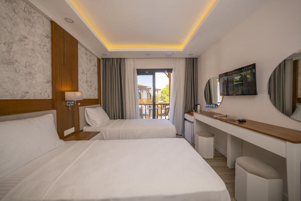A hotel room with two beds, a desk, a TV, and a balcony with outdoor seating.