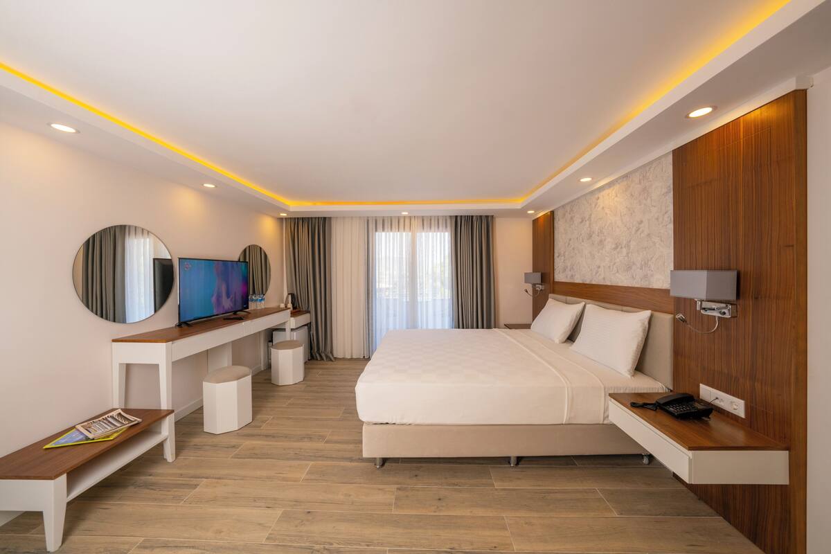 A modern hotel room with a large bed, a TV, a desk, and a small seating area.