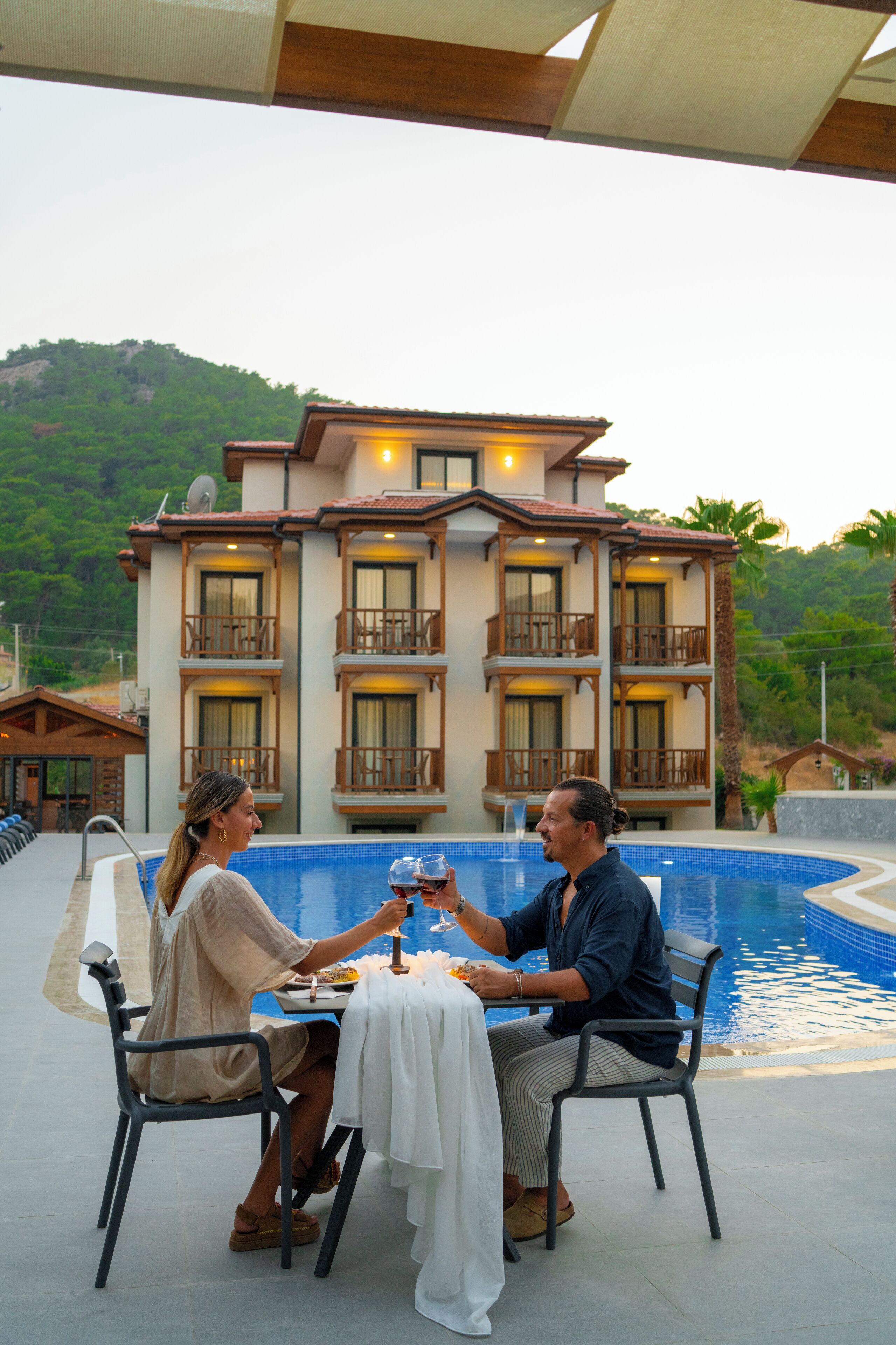 Ein Essbereich mit Tisch und Stühlen am Pool, mit Blick auf einen Pool und ein großes Gebäude mit Balkonen.