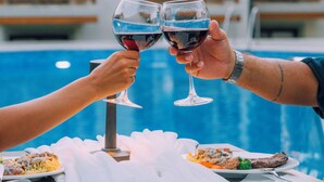 Une table à manger dressée avec un repas et deux verres à vin, le tout placé devant une piscine, avec en arrière-plan un hôtel doté de balcons.