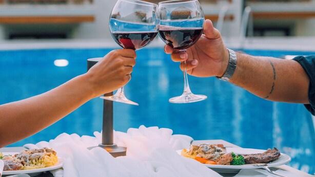 A dining table with a meal and two wine glasses, set against a poolside view of a hotel with balconies. - MARVELOUS SARIGERME (Sarigerme)