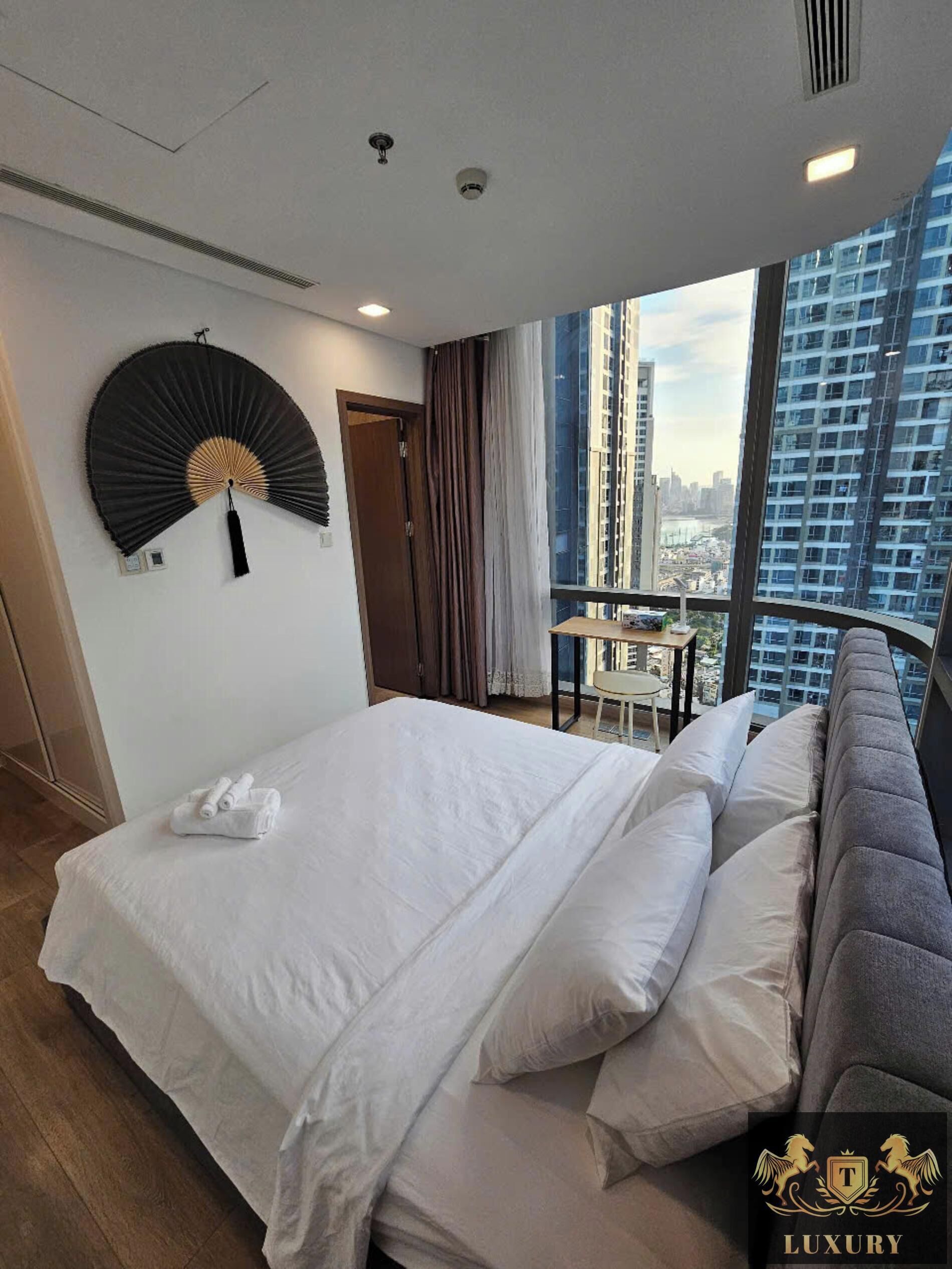 Une chambre d’hôtel avec un lit, un ventilateur, une vue sur la ville et un balcon équipé d’une table et de chaises.