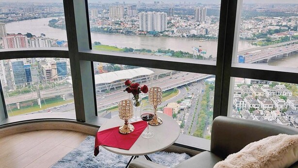 A high-rise room with a large window offering a city view, a round table with a red cloth, and a plush chair with a fur throw. - Landmark 81 Residences Luxury (Ho Chi Minh City)