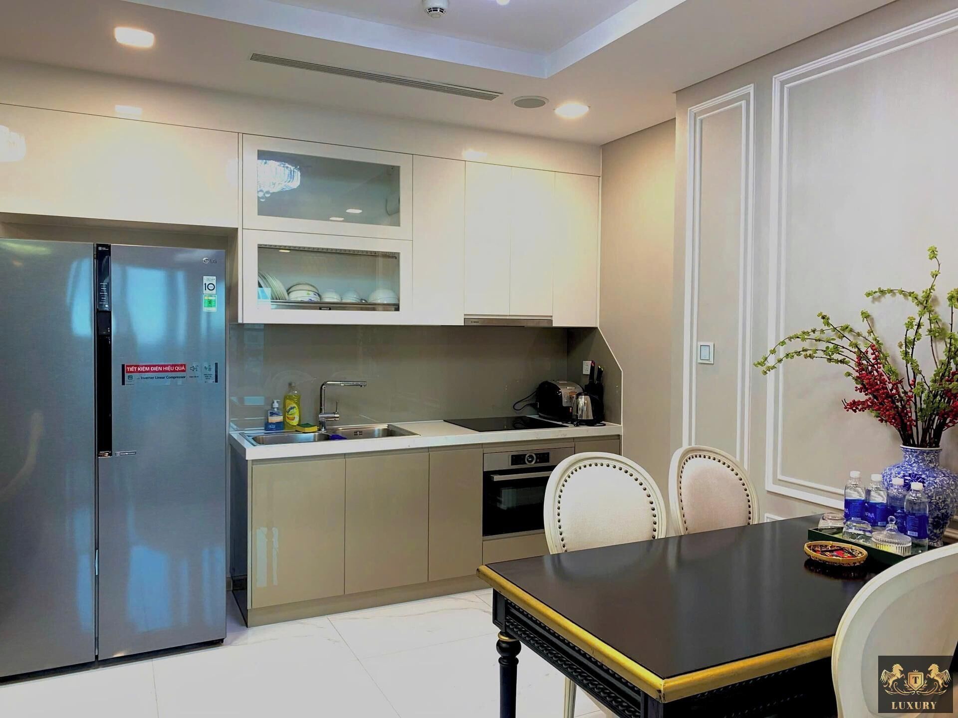A modern kitchen with a stainless steel refrigerator, a sink, and a dining area with a table and chairs.