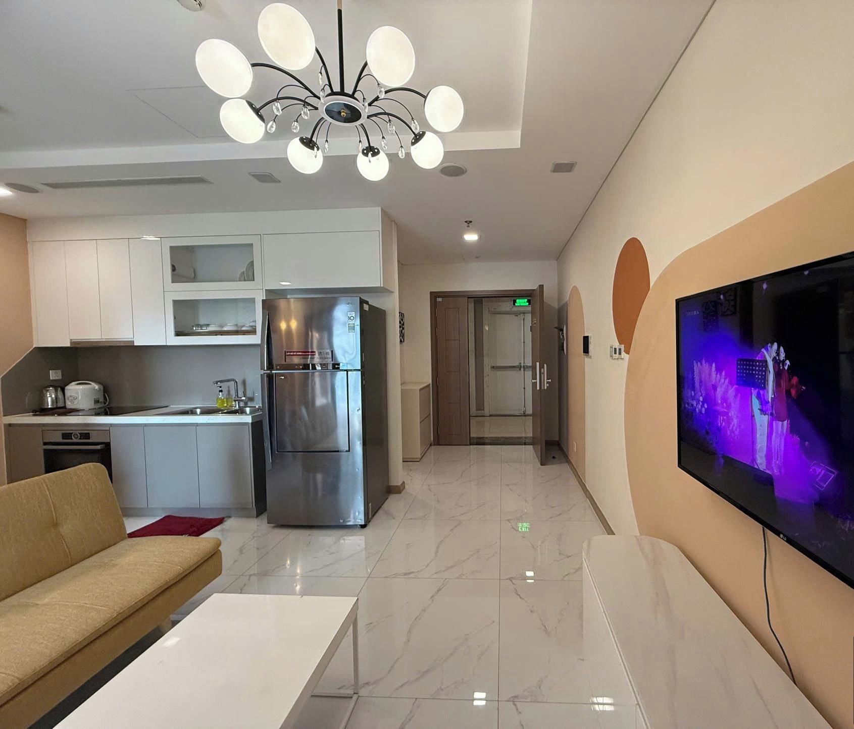 A modern kitchen with a stainless steel refrigerator, a dining area with a white table, and a TV mounted on the wall.